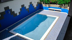 A rectangular swimming pool with a tiled border and a blue and white tiled deck area.