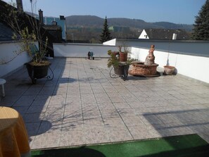 A rooftop terrace with potted plants, a stone fountain, and a view of distant hills. - Hotel Zum Josefshof (Graach)