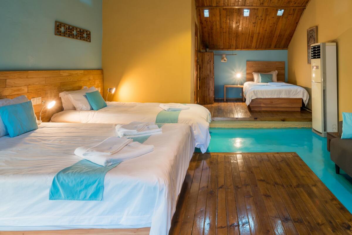 A hotel room with two beds, wooden flooring, a ceiling fan, and an air conditioning unit.