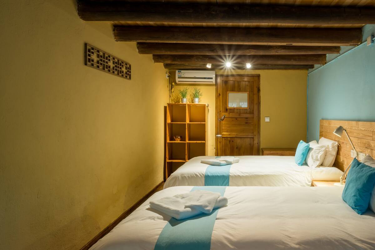 A bedroom with two beds, wooden beams on the ceiling, a wooden wardrobe, and a door with a window.