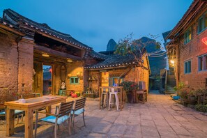 A courtyard with a wooden table and chairs, a reception area, and a staircase leading to an upper level. - The Giggling Tree (Guilin)