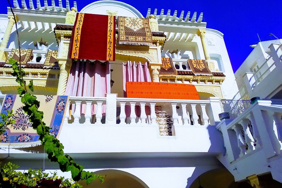 Un bâtiment doté de balcons richement décorés, d’un tissu rouge suspendu et d’une façade blanche.
