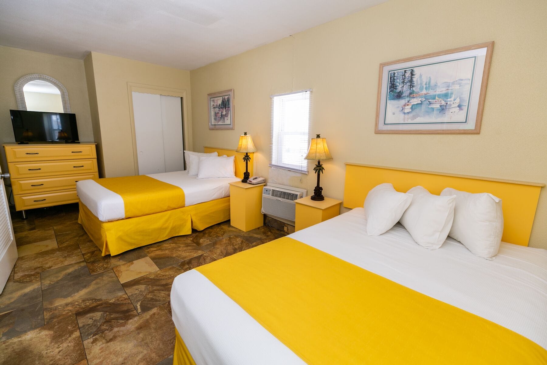 A hotel room with two beds, a TV, a dresser, and artwork on the walls.