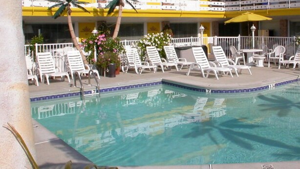 Uma área de piscina com cadeiras de lounge brancas e um guarda-sol amarelo.