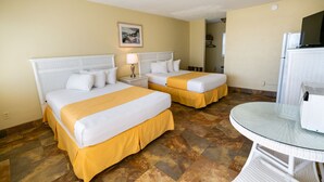 Quarto de hotel com duas camas, uma mesa pequena e um frigorífico.