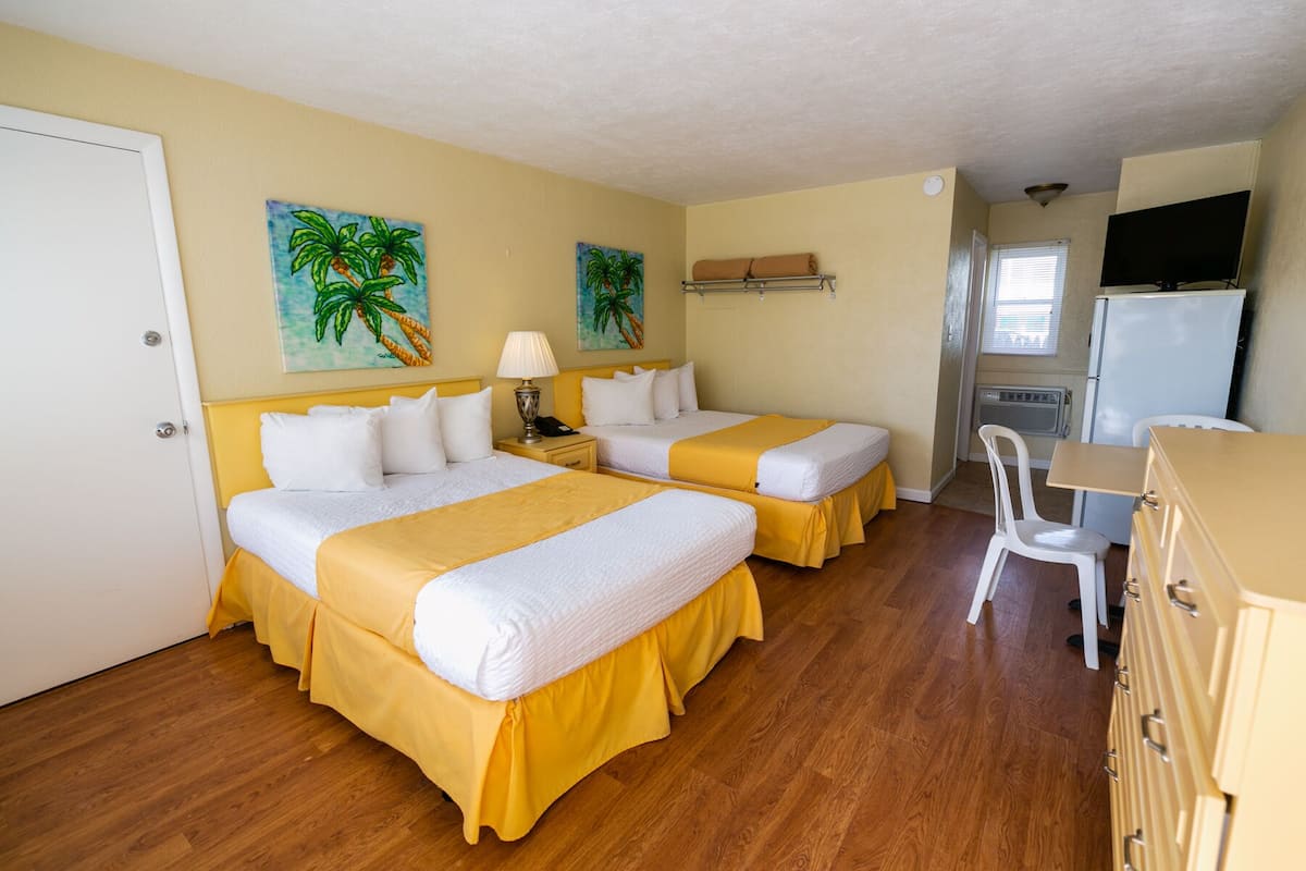 A hotel room with two beds, a desk, a chair, a refrigerator, and two paintings on the wall.