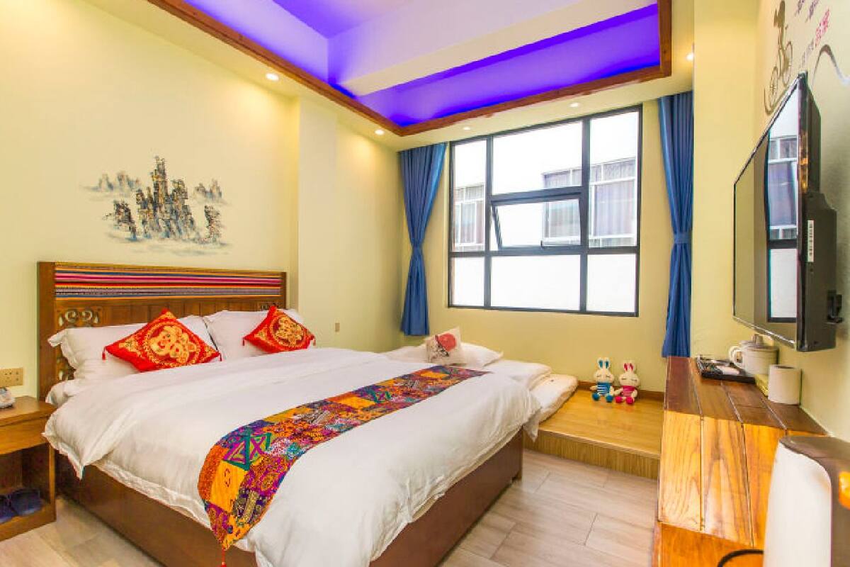 Habitación de hotel con una cama grande, cabecera de madera, televisor de pantalla plana, escritorio con silla y ventana con cortinas.
