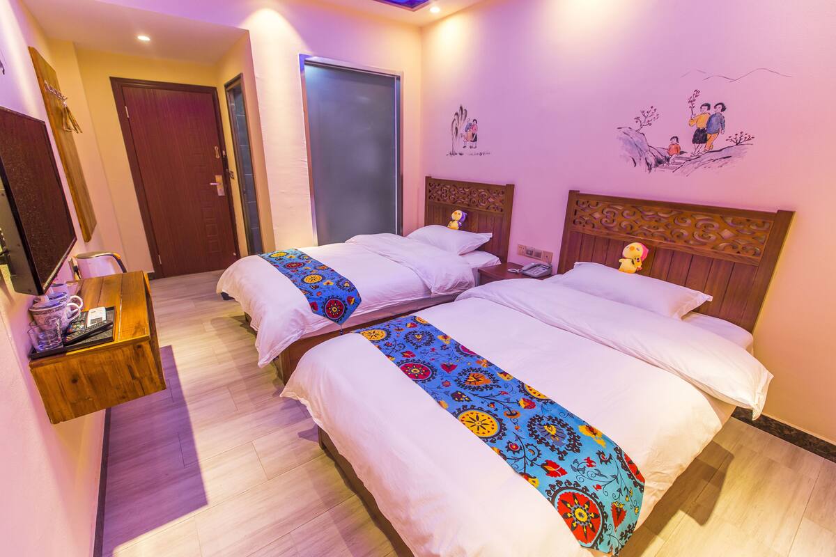 Habitación de hotel con dos camas, cabecero de madera, mesita de noche con lámpara y decoración en la pared.