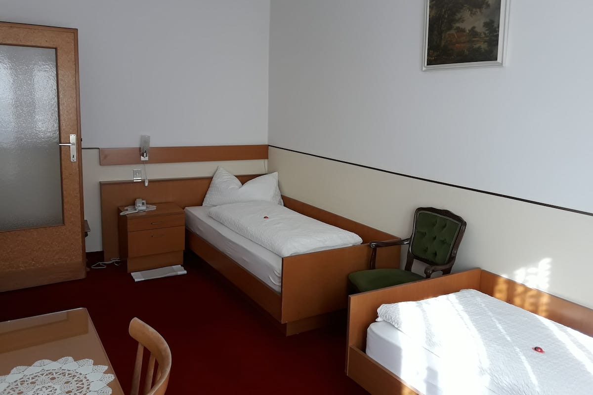 A hotel room with a single bed, a chair, a desk, and a small table.
