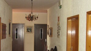 A hallway with a red carpet, a chandelier, and a vintage armchair. There are two doors and a wooden wardrobe. - Hotel Garni Lux (Merano)