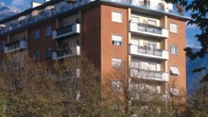 A multi-story apartment building with balconies, surrounded by trees and a clear sky. - Hotel Garni Lux (Merano)