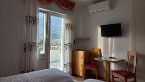 A hotel room with a bed, a desk with a chair, a TV, and a view of the outdoors. - Hotel Garni Lux (Merano)