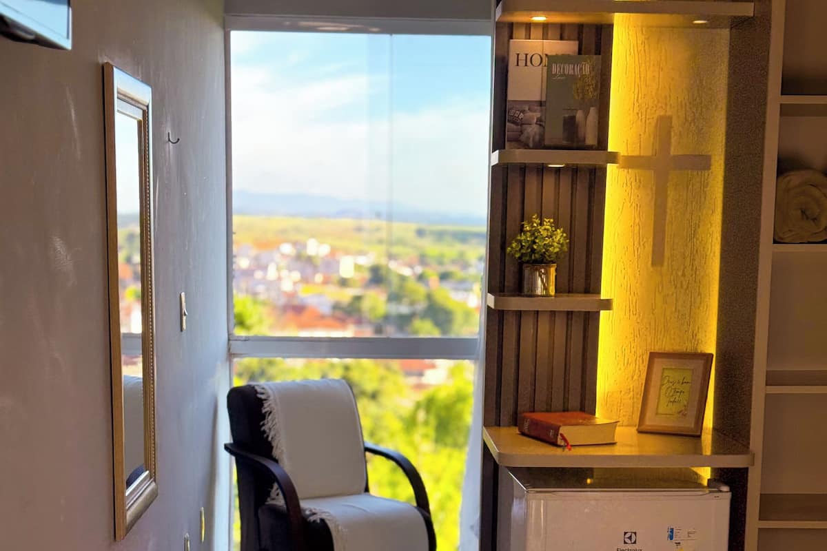 Habitación de hotel con cama, una silla, una mesita con una planta y vista a la ciudad.