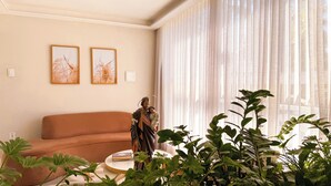 A living room with a brown sofa, two framed pictures on the wall, and a statue on a table. - Pousada do Reinildo (Cachoeira Paulista)