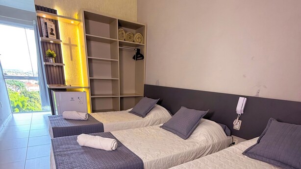 A hotel room with three beds, a wardrobe, and a view of greenery outside. - Pousada do Reinildo (Cachoeira Paulista)