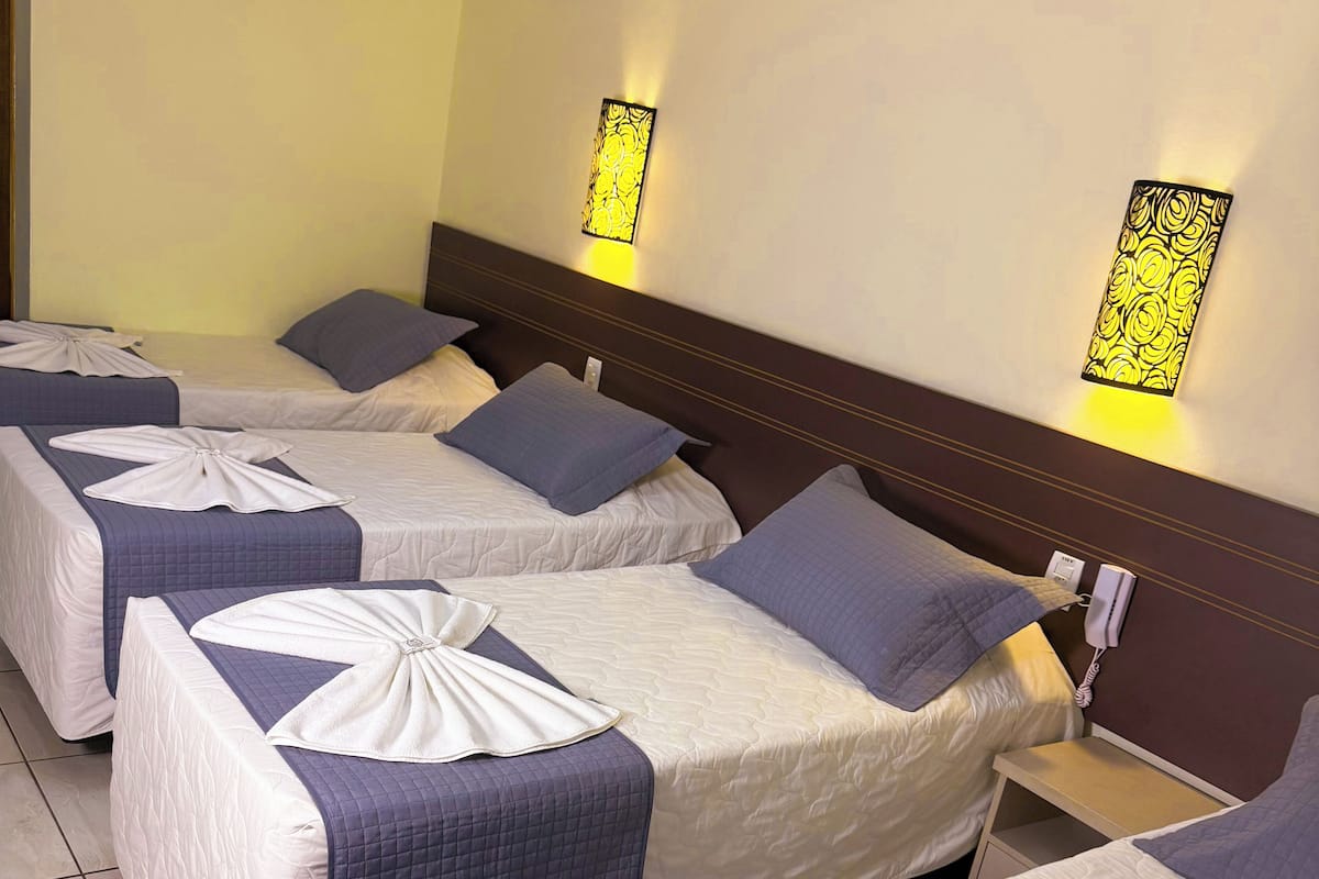 Habitación de hotel con cuatro camas dispuestas en fila, cada una con edredón y almohada.