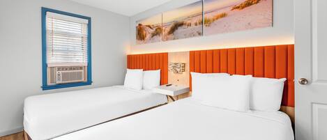 A hotel room with two beds, a large window with blinds, an orange headboard, and a wall-mounted artwork.