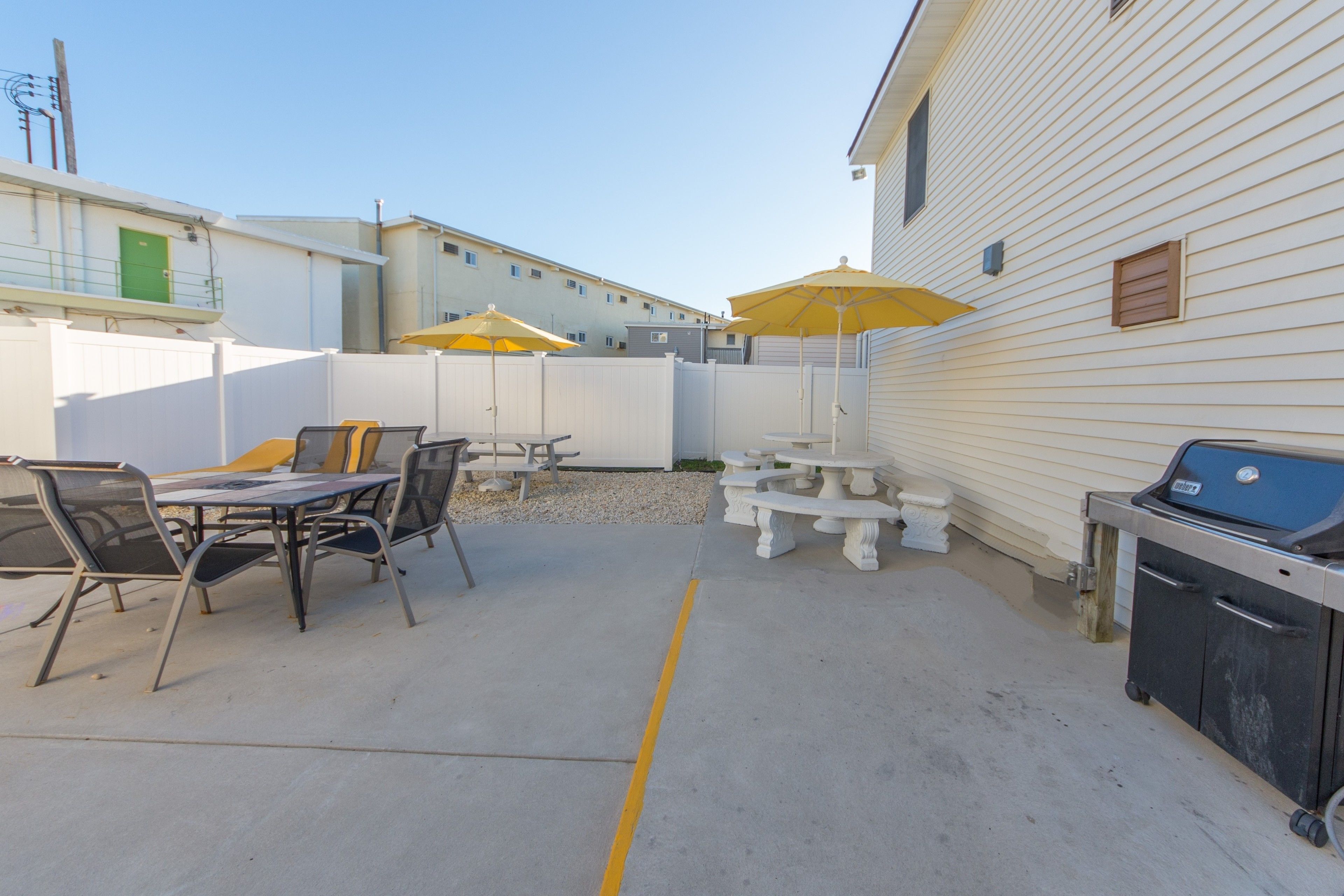 An outdoor patio area with a grill, tables, chairs, and umbrellas.