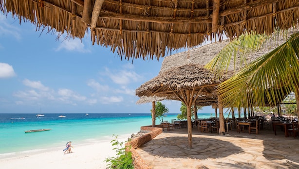 Un resort frente a la playa con una estructura de techo de paja, suelo de piedra y vistas al océano.