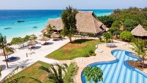 Un resort con piscina, zona de playa y estructuras de techo de paja.