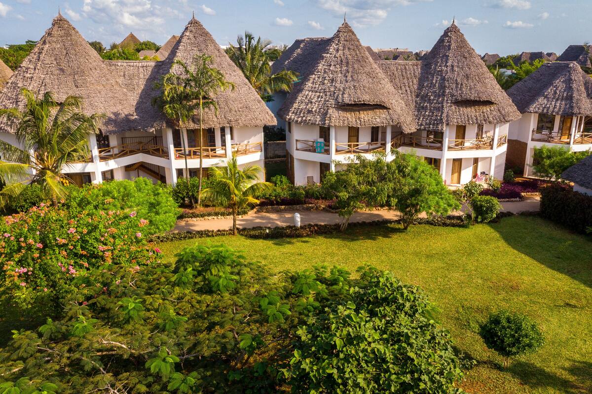 A resort with thatched-roof villas, lush greenery, and a clear sky.