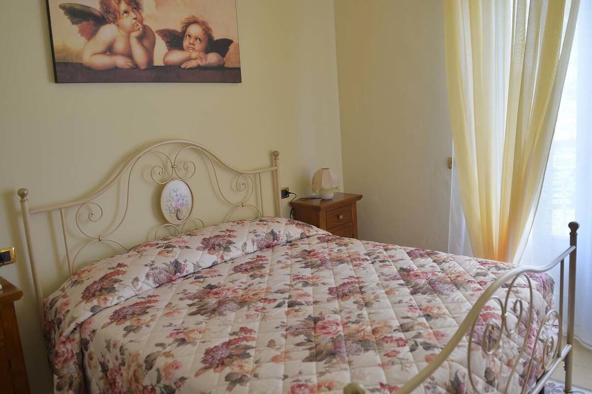 Una camera da letto con una coperta a fiori, un comodino con una lampada e un dipinto di cherubini sulla parete.