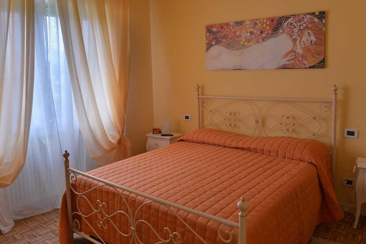 Una camera da letto con un letto, tende, un comodino e un quadro appeso al muro.