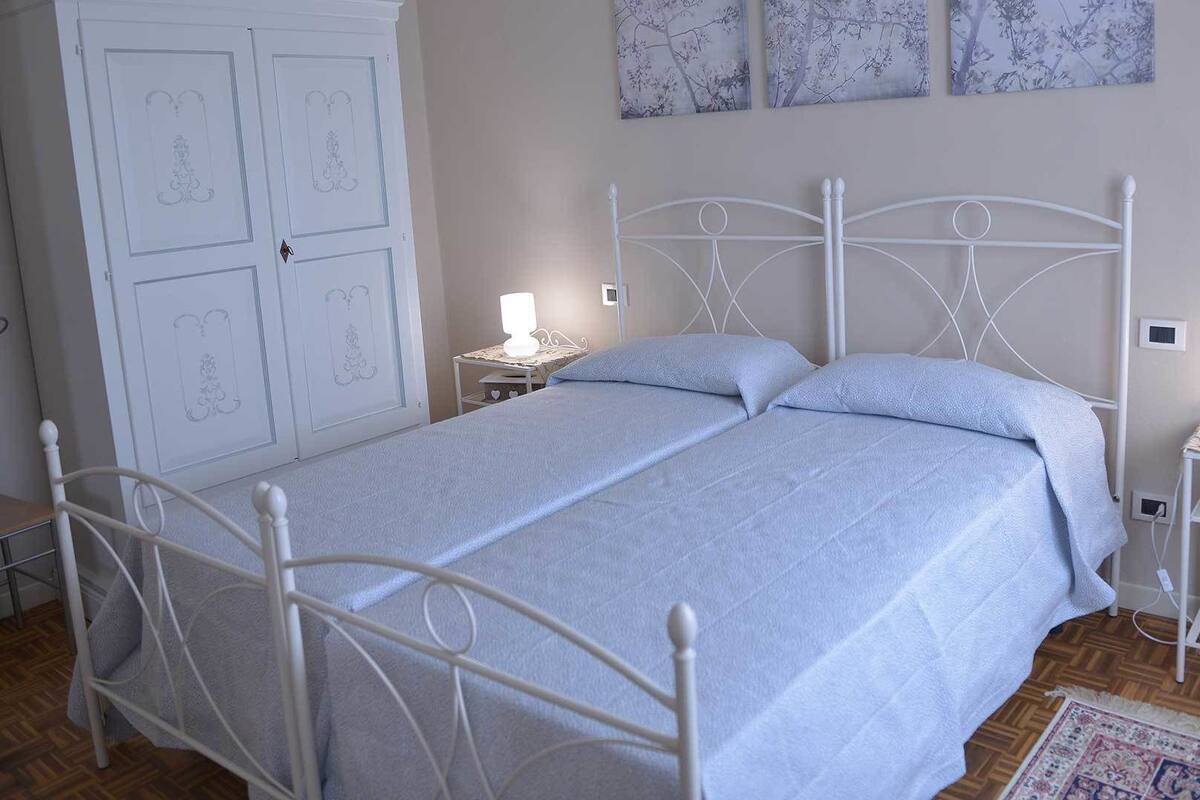 Una camera da letto con un letto in ferro battuto bianco, un comodino con una lampada e un armadio con pannelli decorativi.