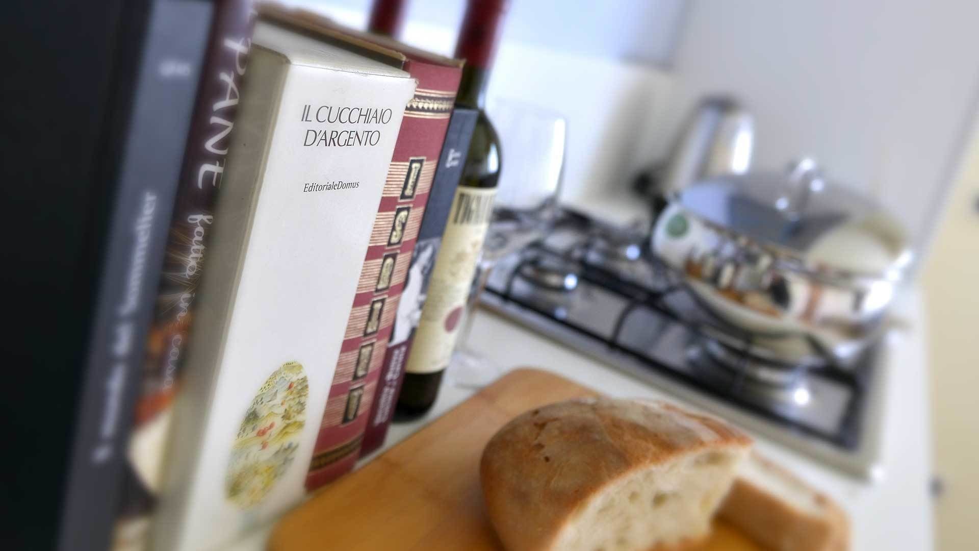 Une cuisine avec une miche de pain sur une planche à découper, une bouteille de vin et une boîte de pâtes.