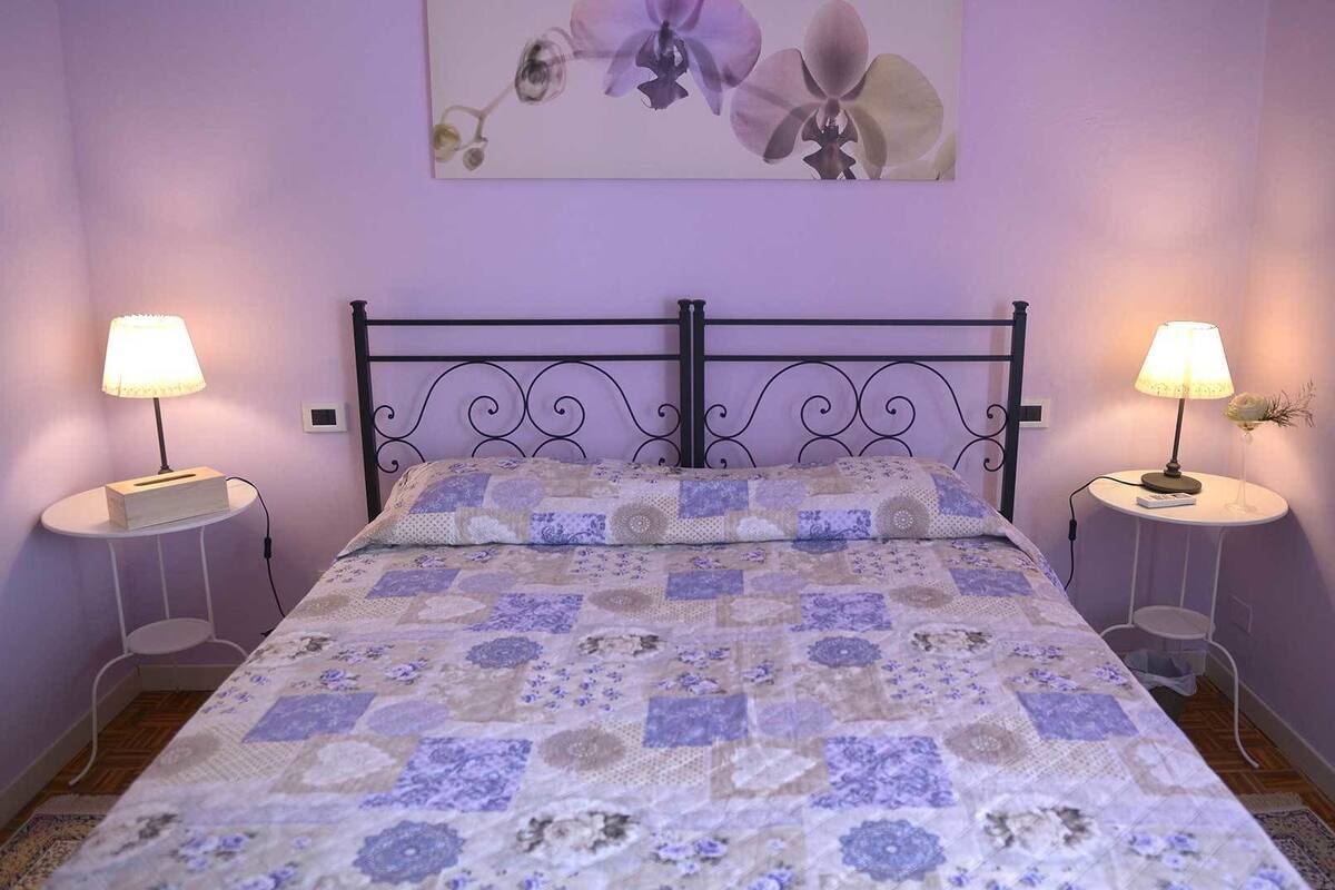Una camera da letto con un letto, due comodini, una lampada a parete e un'opera d'arte floreale.