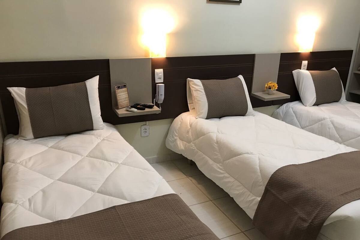 A hotel room with two beds, each with a headboard, bedside tables, and wall-mounted lamps.