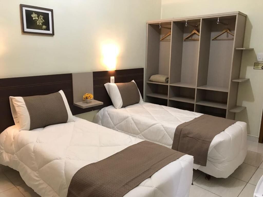 Ein Hotelzimmer mit zwei Betten, einem Nachttisch mit Lampe, einem Kleiderschrank und einem gerahmten Bild an der Wand.