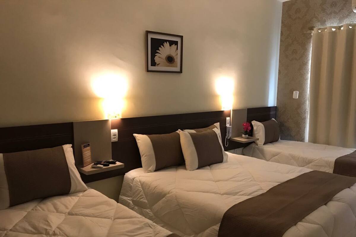 A hotel room with three beds, each with a headboard, bedside tables, and lamps.