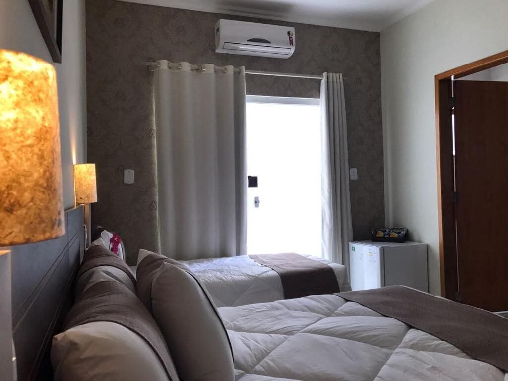 Habitación de hotel con dos camas, una mesita, un aire acondicionado y una puerta.