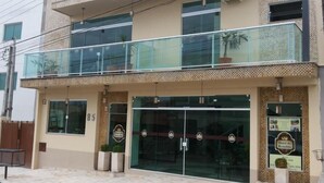 A hotel with a modern design, featuring a glass entrance, a balcony with potted plants, and a signboard advertising the hotel. - Hotel do Reinildo (Cachoeira Paulista)