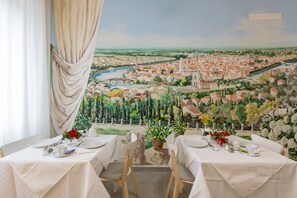 Un espace repas avec des tables préparées pour deux personnes, offrant une vue panoramique sur un paysage urbain avec une rivière et de la verdure.