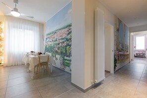 Un coin repas avec une table dressée pour deux personnes, un ventilateur de plafond et une fresque murale représentant un paysage.