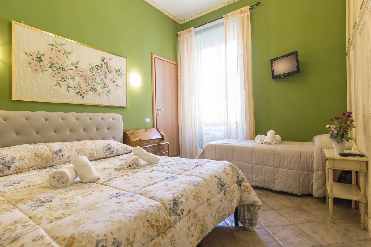A hotel room with a large bed, a smaller bed, a television, and a painting on the wall.