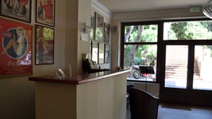 A reception area with a counter, framed posters on the wall, and a view of the outside through large windows. - Akraion (Penteli)