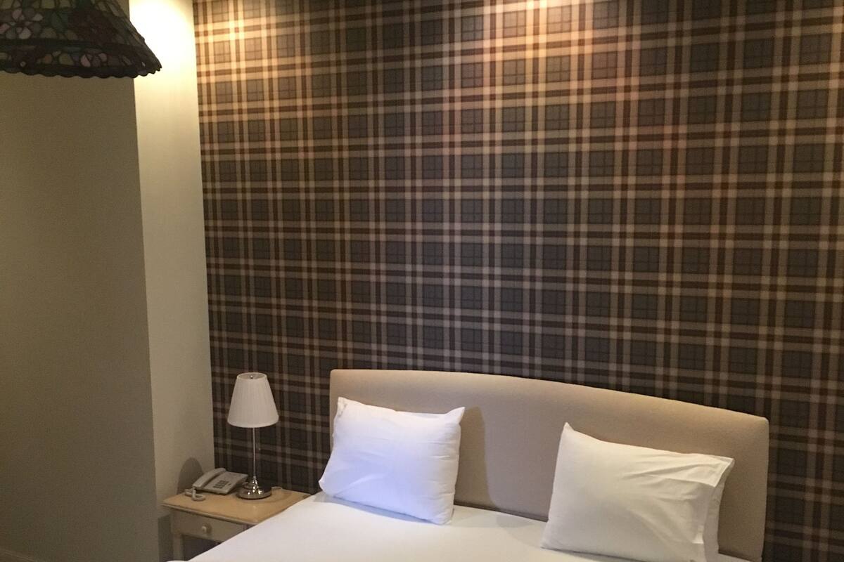 A hotel room with a large bed, a nightstand with a lamp, and a plaid-patterned wall.
