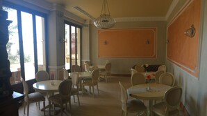 A dining area with round tables and chairs, large windows, and a hanging light fixture. - Akraion (Penteli)