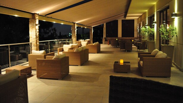 An outdoor lounge area with wicker furniture, a glass balustrade, and a view of the night sky. - Akraion (Penteli)