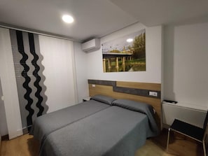 A bedroom with a bed, a wall-mounted air conditioner, a painting of a bridge, and a wooden headboard. - Hostal Rioja Condestable (Logroño)