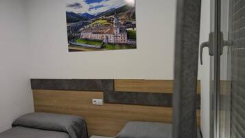 Habitación de hotel con dos camas, cabecero de madera, un cuadro colgado en la pared y una ventana con persianas.