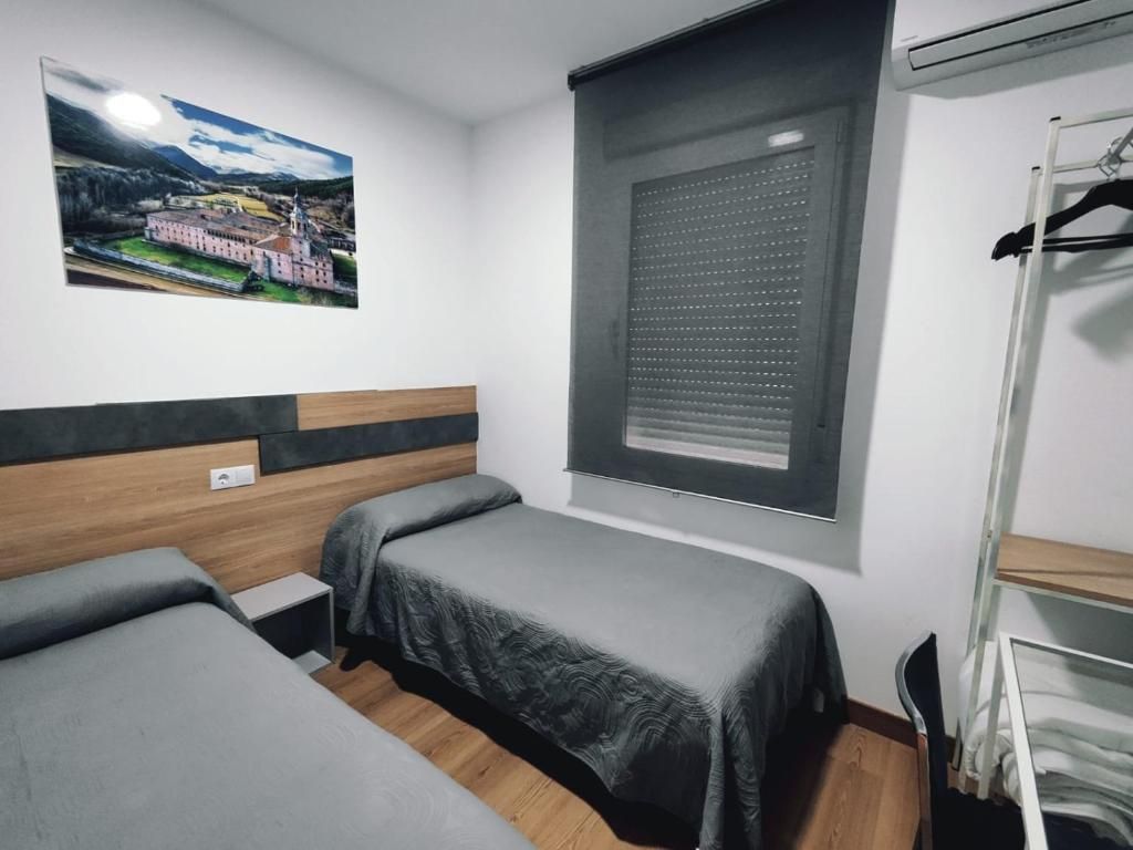 Habitación con dos camas, una ventana con persianas, un perchero y un aire acondicionado instalado en la pared.