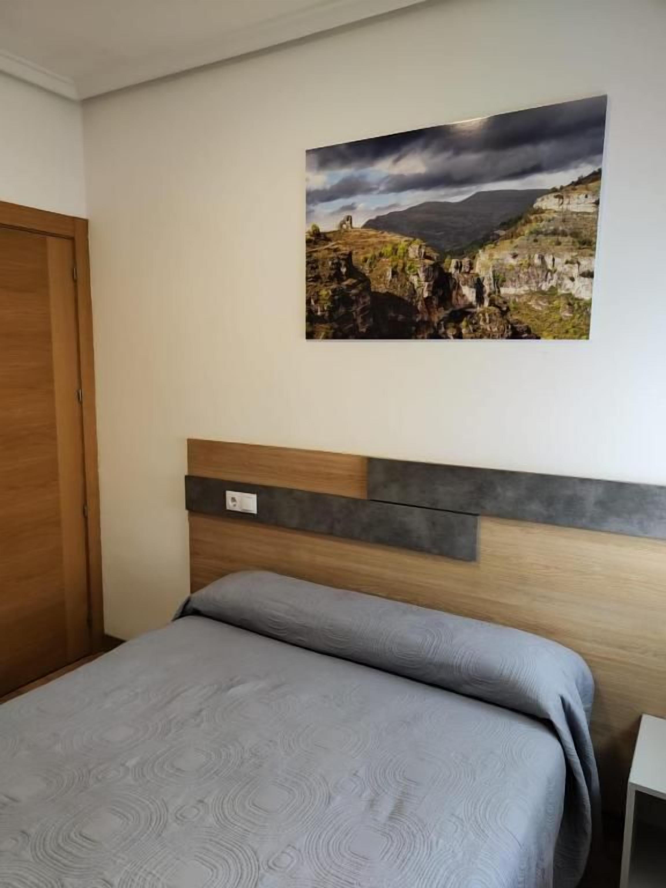 Ein Schlafzimmer mit einem Bett, einem Kopfteil, einem Wandbild und einer Holztür.