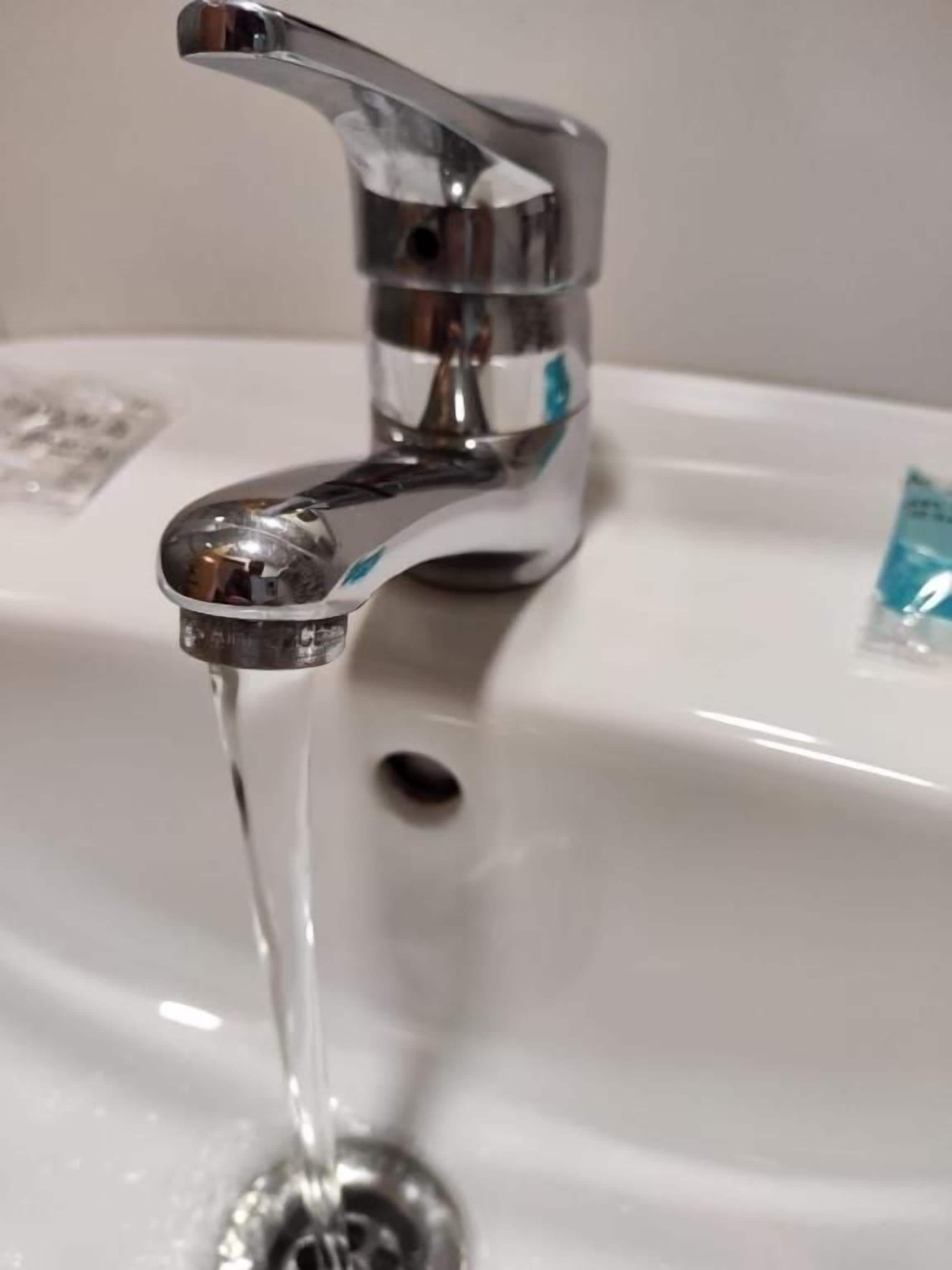 A chrome faucet with water running into a white sink.