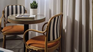 A room with two striped chairs, a small round table with a book and a potted plant, and a window with curtains. - Urban Rooms By Neu Collective (Gzira)