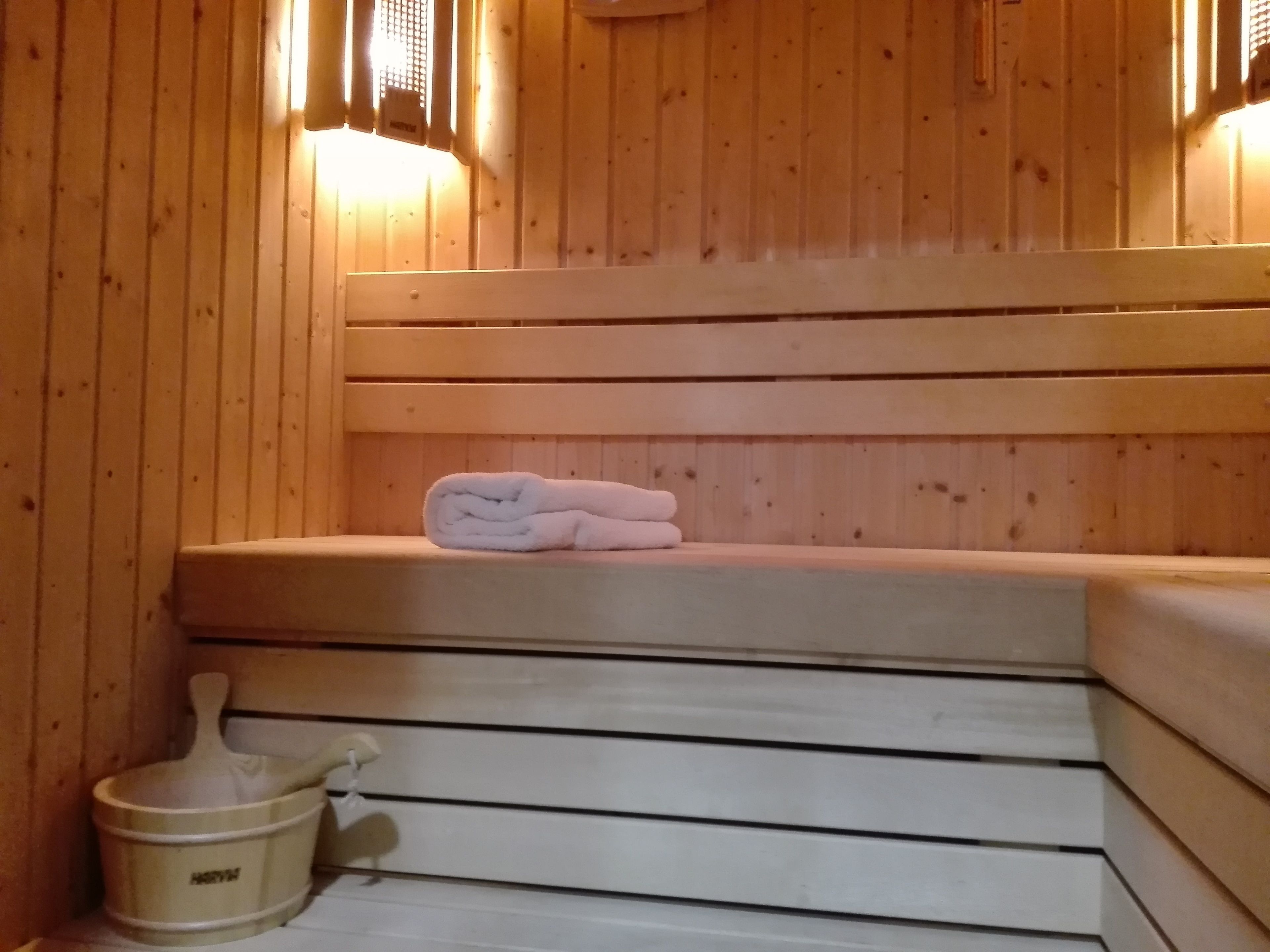 Una sauna de madera con un banco, una toalla y una cuenca de piedra.
