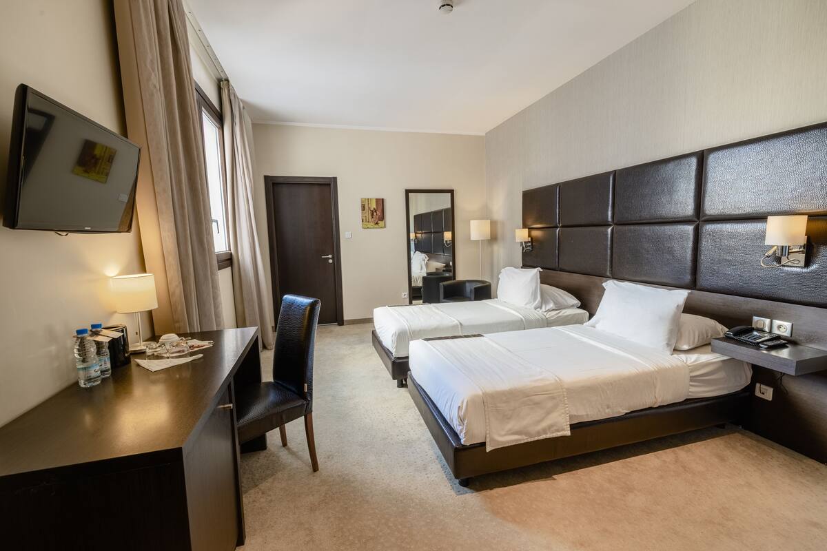 A hotel room with two beds, a desk with a chair, a TV, and a minibar.